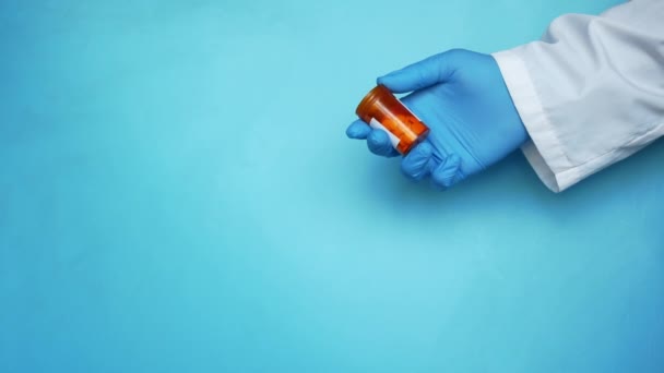 Tangan dokter dalam sarung tangan pelindung memegang pil kontainer terhadap biru — Stok Video
