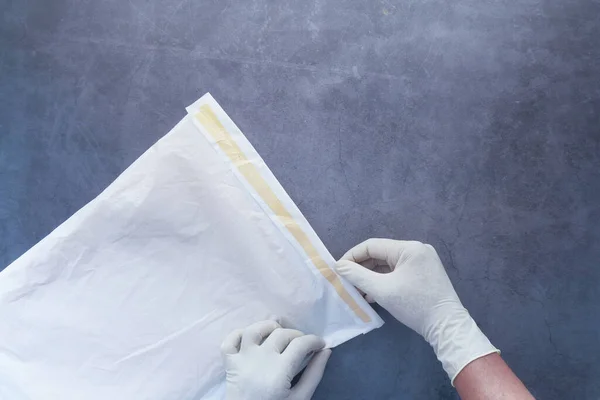 Hand in hand latex handschoenen met witte papieren bubbel envelop voor postschip. — Stockfoto