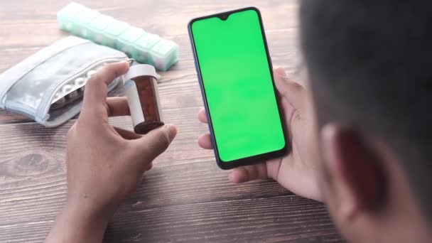 Rear view of young man using smart phone and holding medical pill container — Stock Video