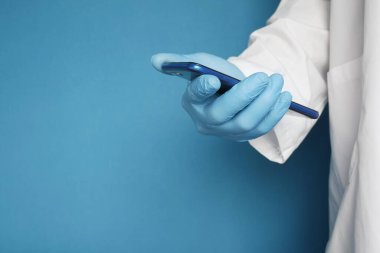 Doktorlar mavi arka planda akıllı telefon kullanarak koruyucu eldivenler veriyorlar. 