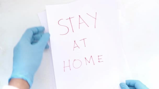 Tangan dokter dalam sarung tangan lateks memegang kertas tertulis tinggal di rumah . — Stok Video