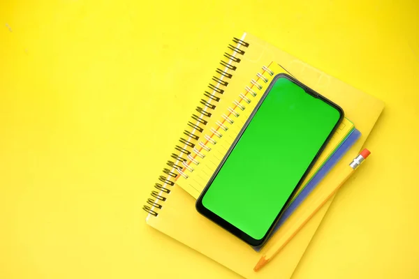 top view of smart phone and yellow color notepad on table