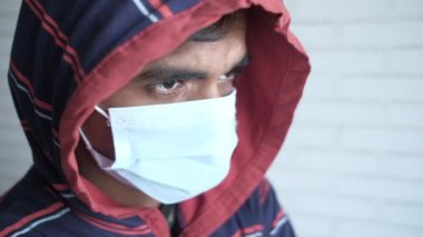 Duvara karşı koruyucu maskeli kapüşonlu genç bir adam. 