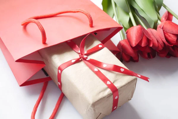 Подарункова коробка в торговому пакеті і червоний тюльпан квітка на столі — стокове фото