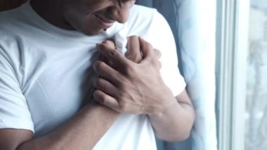 Genç adam kalp ağrısı çekiyor ve göğsünü eliyle tutuyor. 