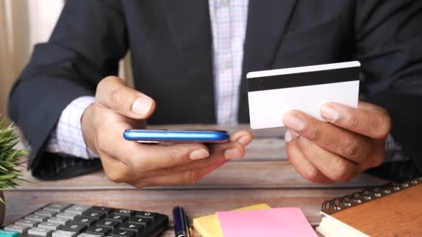 Uomo mano in possesso di carta di credito e utilizzando lo smartphone mentre si trova sulla scrivania dell'ufficio — Video Stock