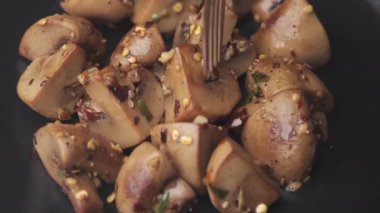 Sarımsak ve maydanozlu sotelenmiş mantarlar beyaz arka planda siyah bir tabakta. 