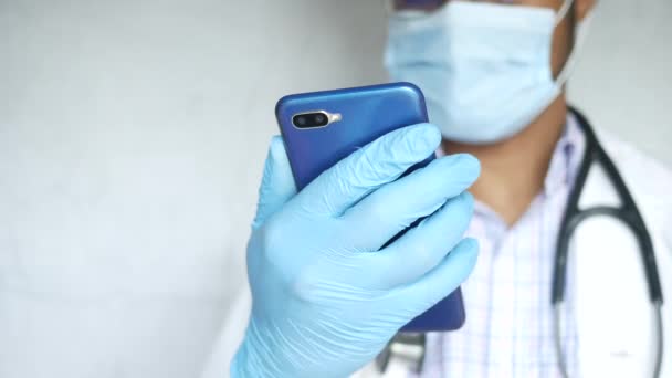 Dokter bertopeng wajah memegang smartphone. — Stok Video