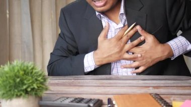 İş adamı kalp acısı çekiyor ve göğsünü eliyle tutuyor. 