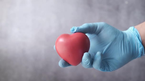 Человек рука в защитных перчатках держа красное сердце на черном фоне — стоковое видео