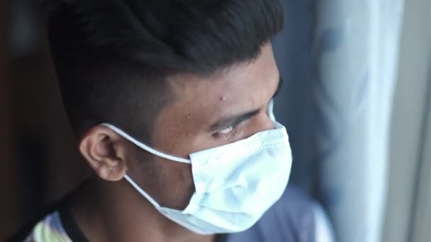 Молодой человек в защитной маске смотрит в окно — стоковое видео