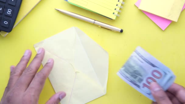 Osoba wkładająca gotówkę do koperty na żółtym tle — Wideo stockowe