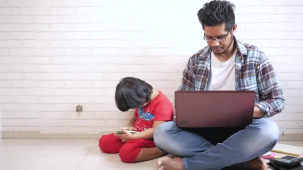 Young father working at laptop at home while child using smart phone on floor — Stock Video