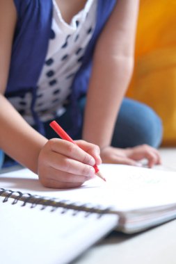 Kağıda çizim yapan kız çocuğu yere oturuyor. 