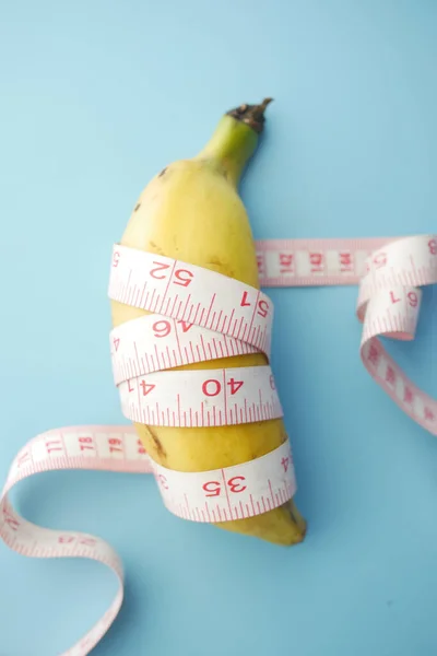close up of measurement tape and banana on blue background