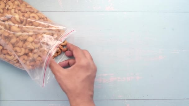 Hand pflückt Cashewnuss aus einer Plastiktüte auf dem Tisch — Stockvideo