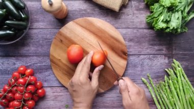 top view of mans hand cutting fresh tomato on chopping board 