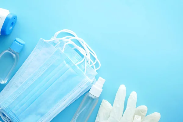 Mascarillas quirúrgicas, termómetro y desinfectante de manos sobre fondo azul —  Fotos de Stock