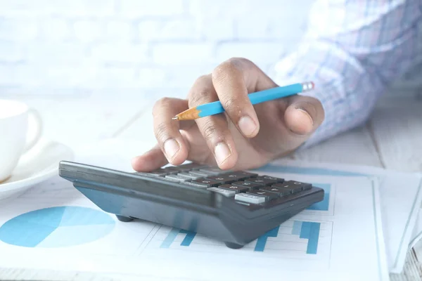 Primer plano de la mano del hombre utilizando la calculadora con datos financieros en la tabla — Foto de Stock