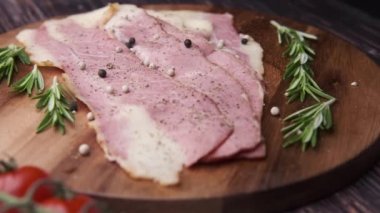 Doğrama tahtasında çiğ domuz pastırması şeritleri, otlar ve domates. .