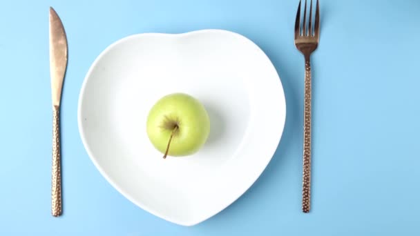 Bestek en leeg bord met groene appel op blauwe achtergrond — Stockvideo