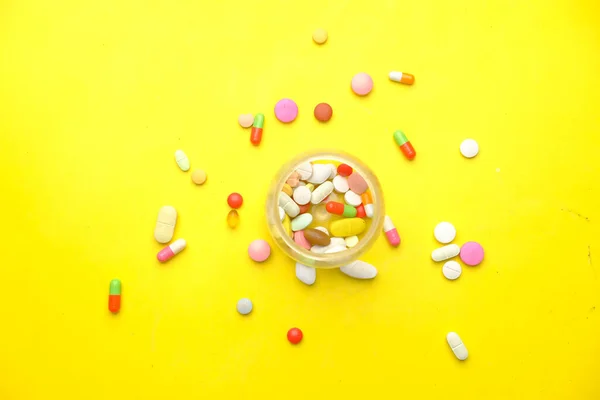 Gros plan de nombreuses pilules et capsules colorées sur jaune — Photo