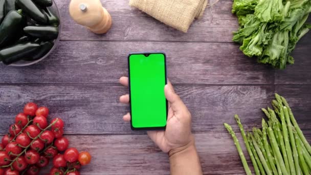Vista superior dos homens mão segurando telefone inteligente com vegetais frescos na mesa — Vídeo de Stock