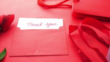 Kırmızı arka planda teşekkür mesajı, hediye ve lale çiçeği zarfı. 