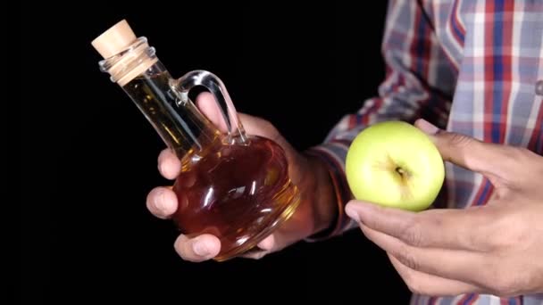Ruční držení jablečný ocet ve skleněné láhvi izolované na černé — Stock video