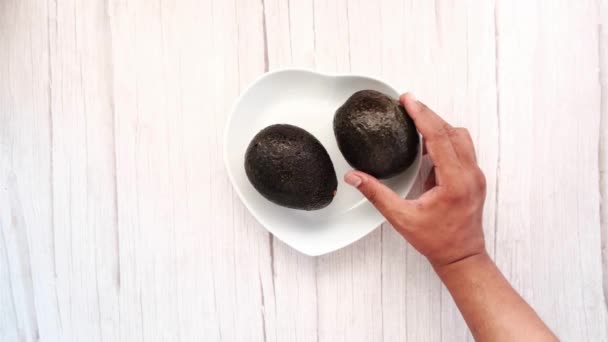 Ручной выбор авокадо из тарелки на деревянном столе — стоковое видео
