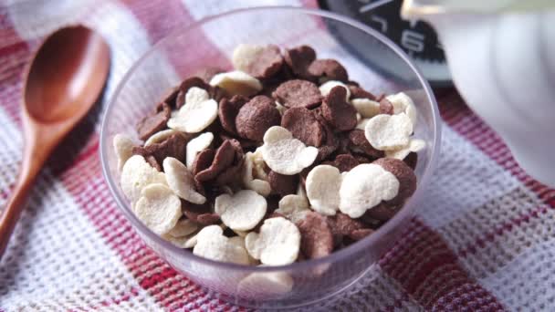 Menuangkan susu ke dalam sereal coklat jagung serpih dalam mangkuk di atas meja — Stok Video