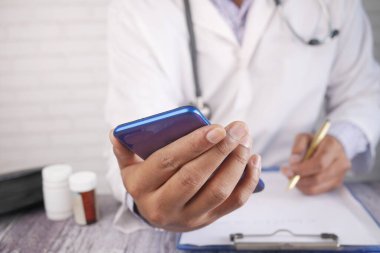 Beyaz önlüklü doktor akıllı telefon kullanıyor ve reçete yazıyor. 