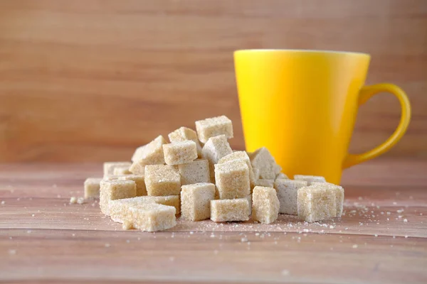 Gele koffiemok en bruine suikerklontje op tafel — Stockfoto