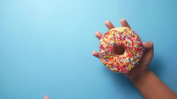 Дитяча рука тримає пончики на синьому фоні — стокове відео