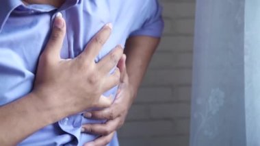 Genç adam kalp ağrısı çekiyor ve göğsünü eliyle tutuyor. 