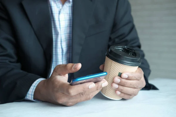 Mano de hombre de negocios usando teléfono inteligente y taza de café de papel — Foto de Stock
