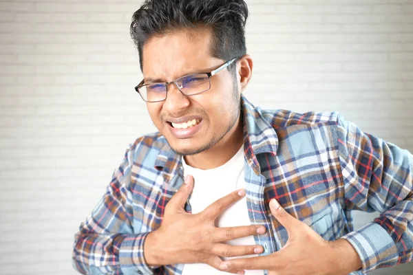 Jonge man lijden pijn in het hart en houden borst met de hand — Stockfoto