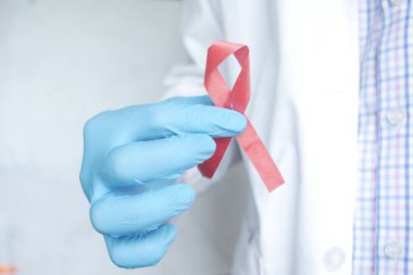 Doktor eli pembe renk HIV kurdelesini tutuyor. Yakın plan. 