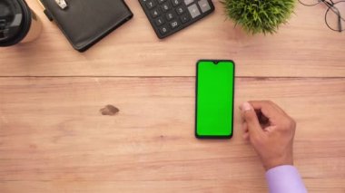 Adam ofis masasındaki modern akıllı telefona el sallıyor. 