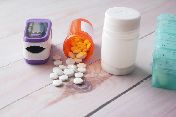 pulse oximeter, medical pills and container on table 