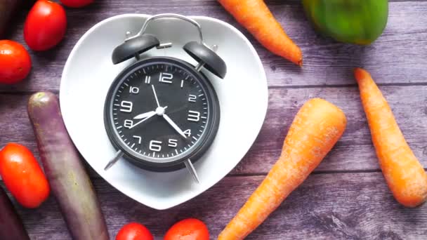 Свежие овощи и будильник на тарелке в форме сердца на столе — стоковое видео