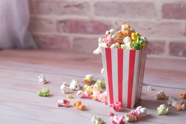 Popcorn verschüttet aus einem Papiercontainer auf hölzernem Hintergrund — Stockfoto