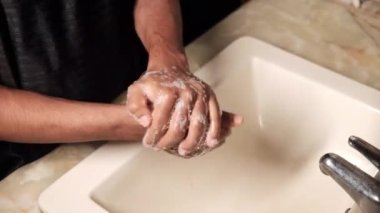 Genç adam ellerini sabunla sıcak suyla yıkıyor. 