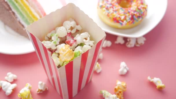 Торт, пончики и попкорн в бумажном контейнере на розовом — стоковое видео