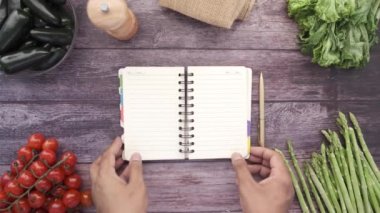 Masada taze sebzeyle sayfaları çeviren insanların el görüntüsü. 