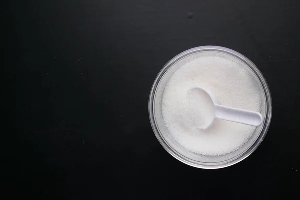 Witte suiker en lepel in een container op zwarte achtergrond, — Stockfoto