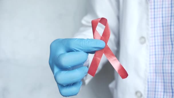 Main dans les gants médicaux tenant le ruban rouge du VIH haut vers le bas — Video