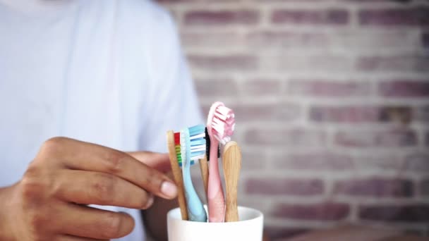 Handplockning färgglada tandborstar i vit mugg mot en vägg — Stockvideo