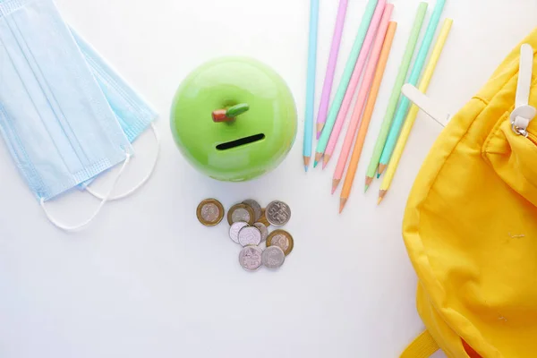 Lápices de color, mascarilla y monedas sobre fondo blanco — Foto de Stock