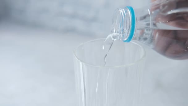 Наливать воду из пластикового контейнера в стекло на стол — стоковое видео